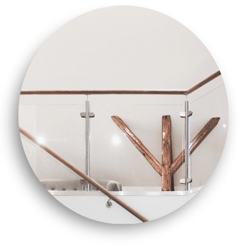 Sisäkäyttöön tarkoitettu lasikaide, jossa on ruostumattomat tolpat ja puinen käsijohde. Kaide rajoittaa avointa tilaa, ja puuyksityiskohdat tuovat lämpöä ja luonnollista tunnelmaa sisustukseen.