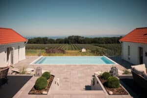 Moderni tolpaton lasiaita infinity-altaan ympärillä – näkymä merelle, omenatarhaan ja avaraan maastoon.