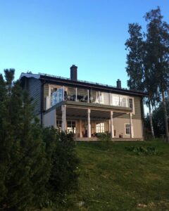 Alumiininen lasikaide asennettuna kaksikerroksisen talon parvekkeelle, alla oleskelutila pylväiden suojassa.