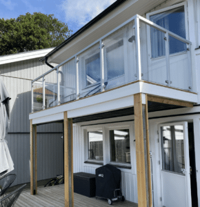 Lasikaide valkoisilla neliönmuotoisilla alumiinitolpilla parvekkeella, puulattia ja puujulkisivu.