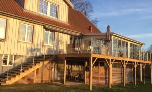 Lasikaide ruostumattomasta teräksestä ja kirkas lasi, asennettu portaisiin ja puuterassille, vieressä ulkohuone ja aurinkoinen julkisivu